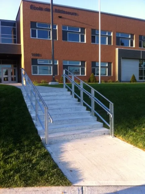 Escalier extérieur en béton bordé de rampes en métal, devant l'École des Bâtisseurs